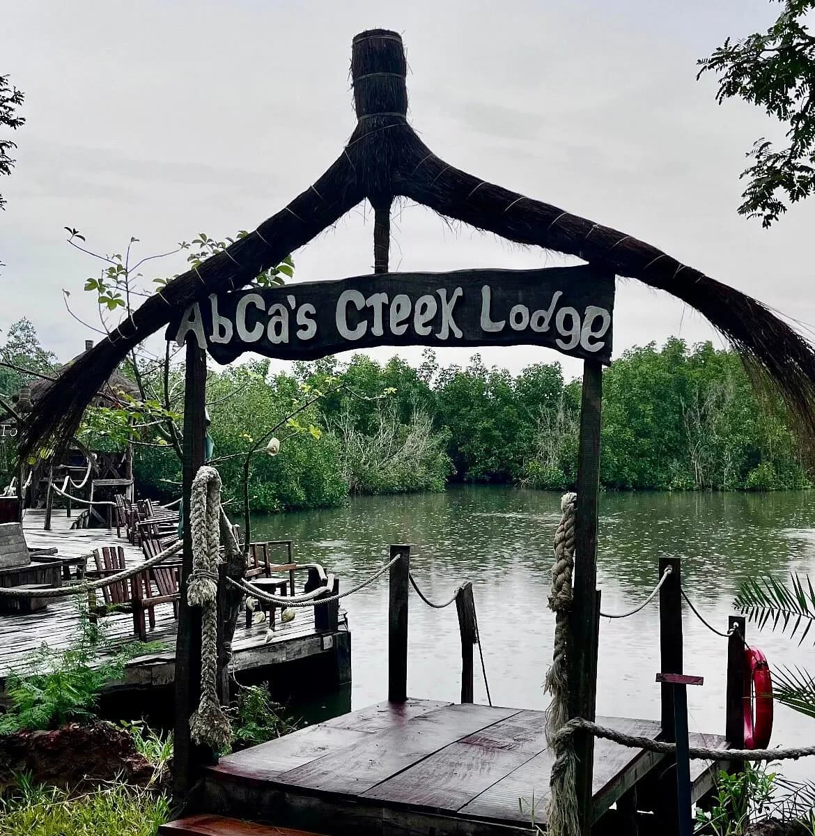 The thatched entrance sign and jetty at AbCa's Creek Lodge beside mangroves